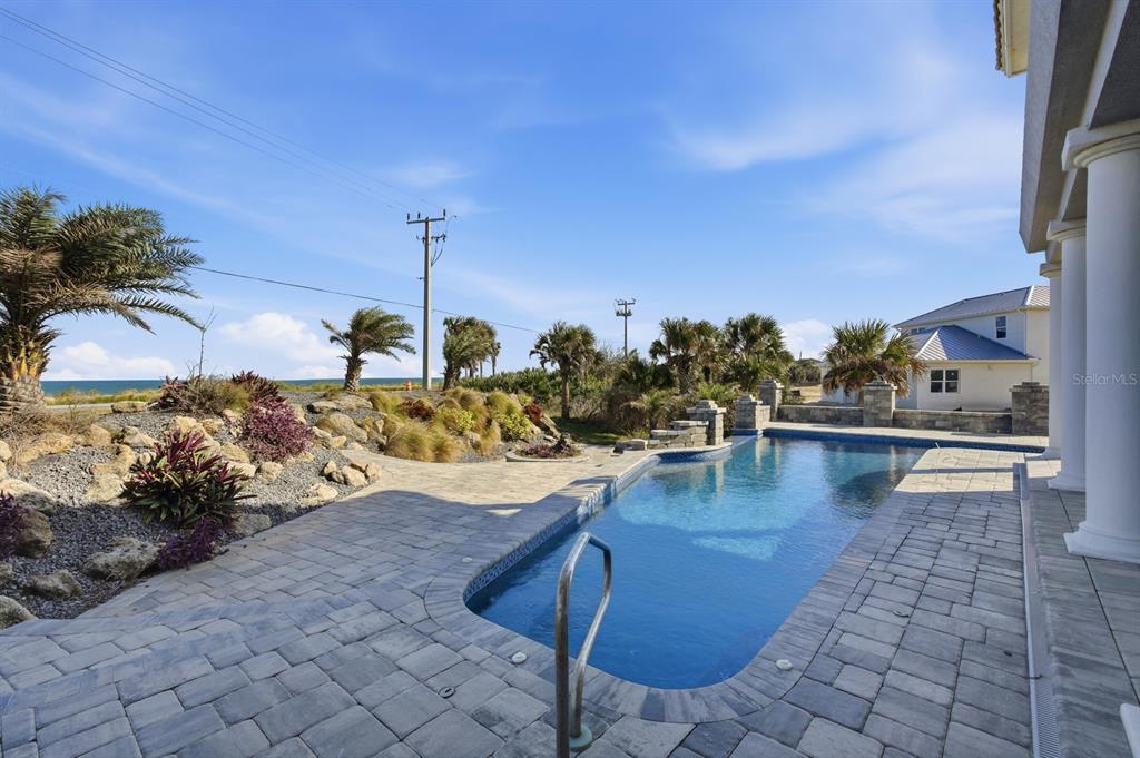 A rectangular swimming pool sits on a stone patio next to a house by the ocean — 100 SANDPIPER RIDGE DRIVE, ORMOND BEACH, FL