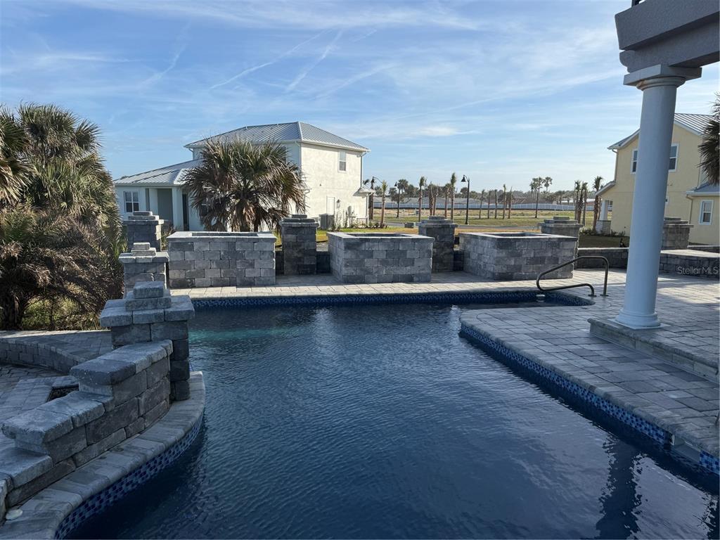A swimming pool with stone pavers and decorative masonry walls in a residential backyard — 100 SANDPIPER RIDGE DRIVE, ORMOND BEACH, FL