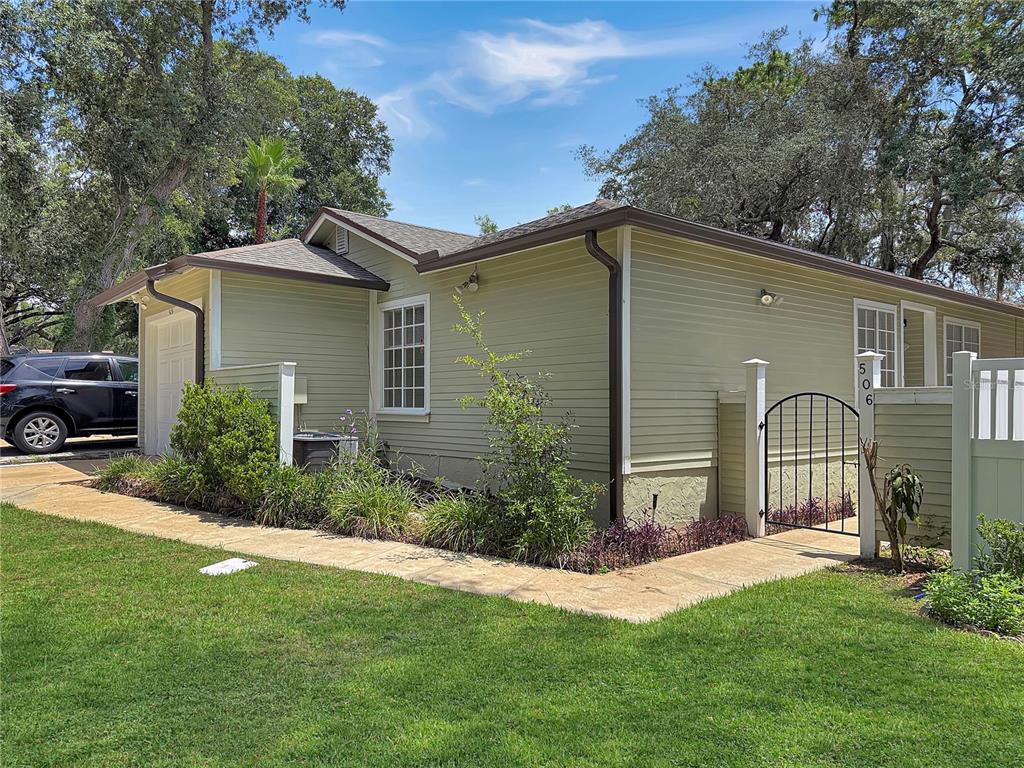 A light green house exterior features a garage, a small gated walkway, and landscaping — 506 HARVARD PLACE, APOPKA, FL