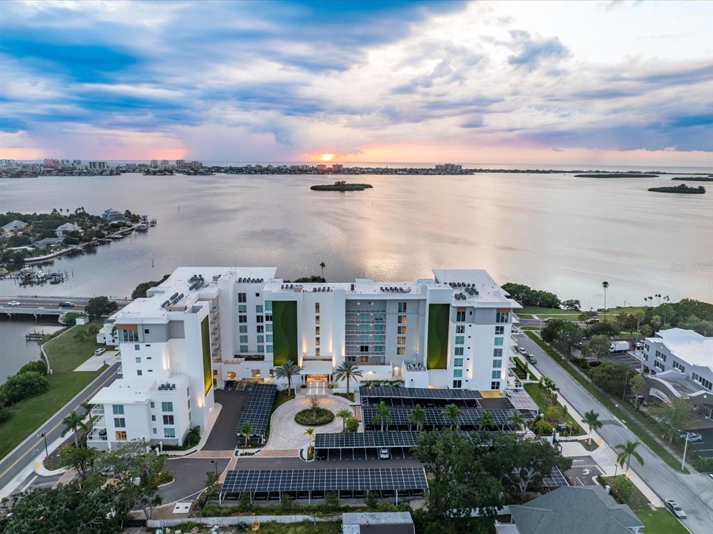 An aerial view of a multi-story apartment building with solar-covered parking lots near water — 1020 SUNSET POINT ROAD UNIT 511, CLEARWATER, FL