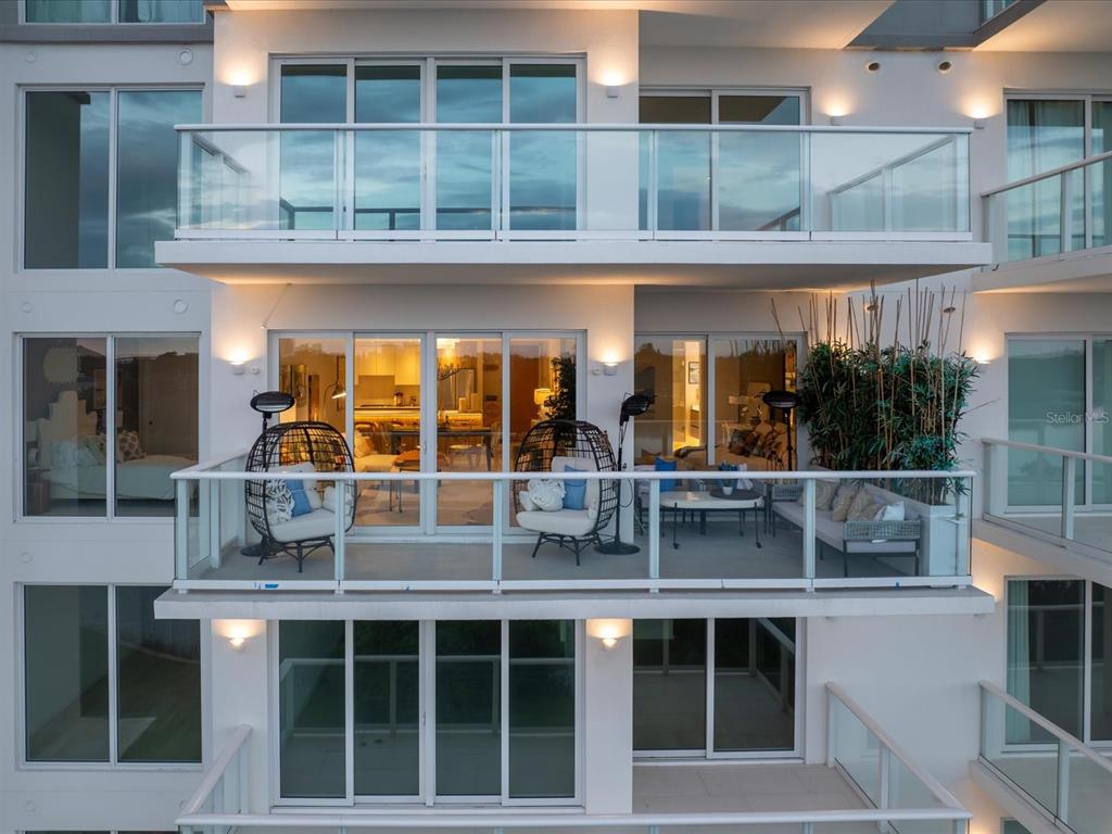 An exterior view of a multi-story building featuring balconies with glass railings and outdoor furniture — 1020 SUNSET POINT ROAD UNIT 511, CLEARWATER, FL