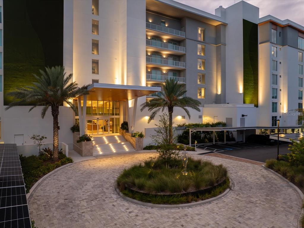 An exterior view of a modern hotel entrance with a circular driveway and palm trees — 1020 SUNSET POINT ROAD UNIT 511, CLEARWATER, FL