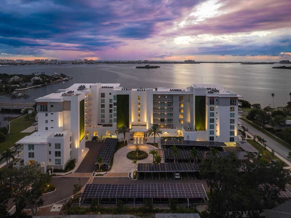 An aerial view of a modern multi-story apartment building with solar-covered parking lots at sunset — 1020 SUNSET POINT ROAD UNIT 511, CLEARWATER, FL