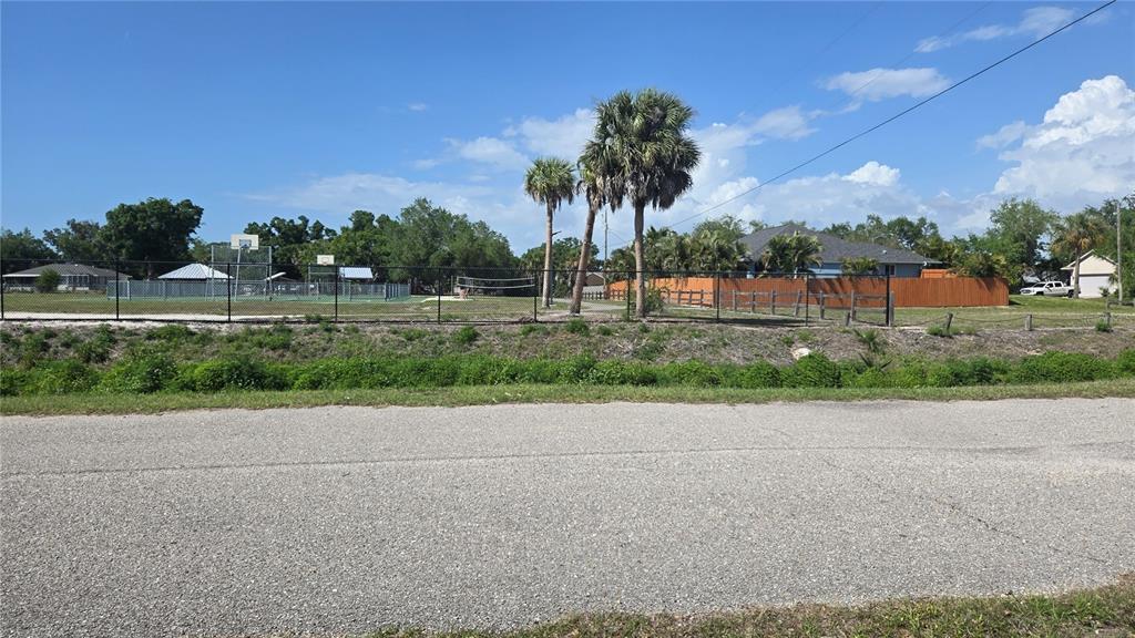 A paved road sits in front of a fenced recreational area with palm trees — ROLLA ROAD, VENICE, FL
