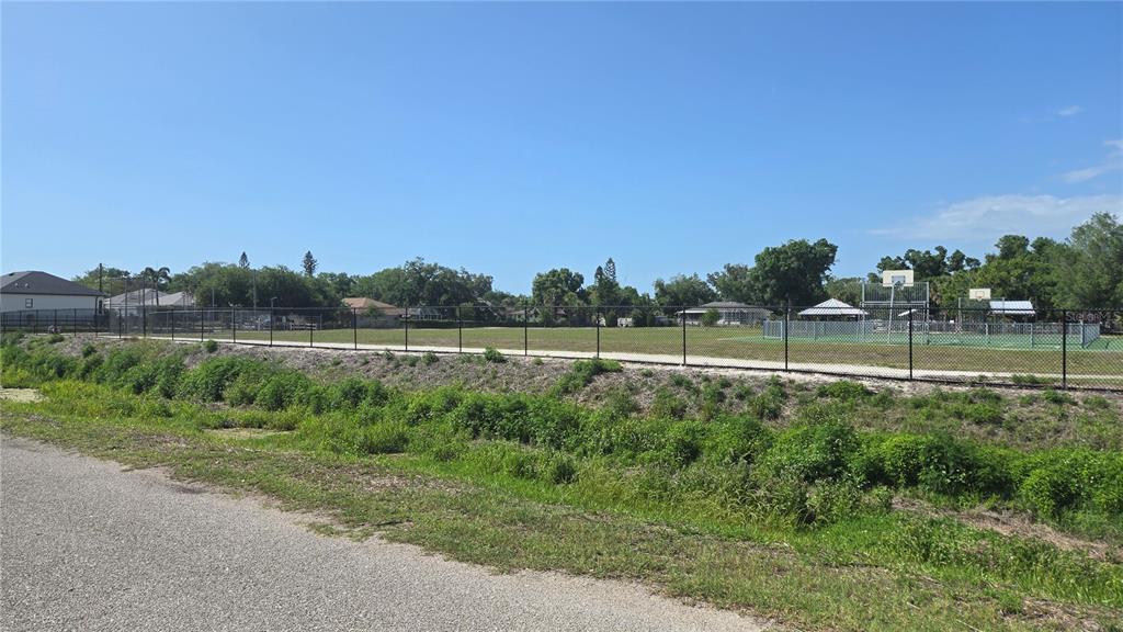 A fenced grassy park with a basketball court sits next to a gravel path — ROLLA ROAD, VENICE, FL