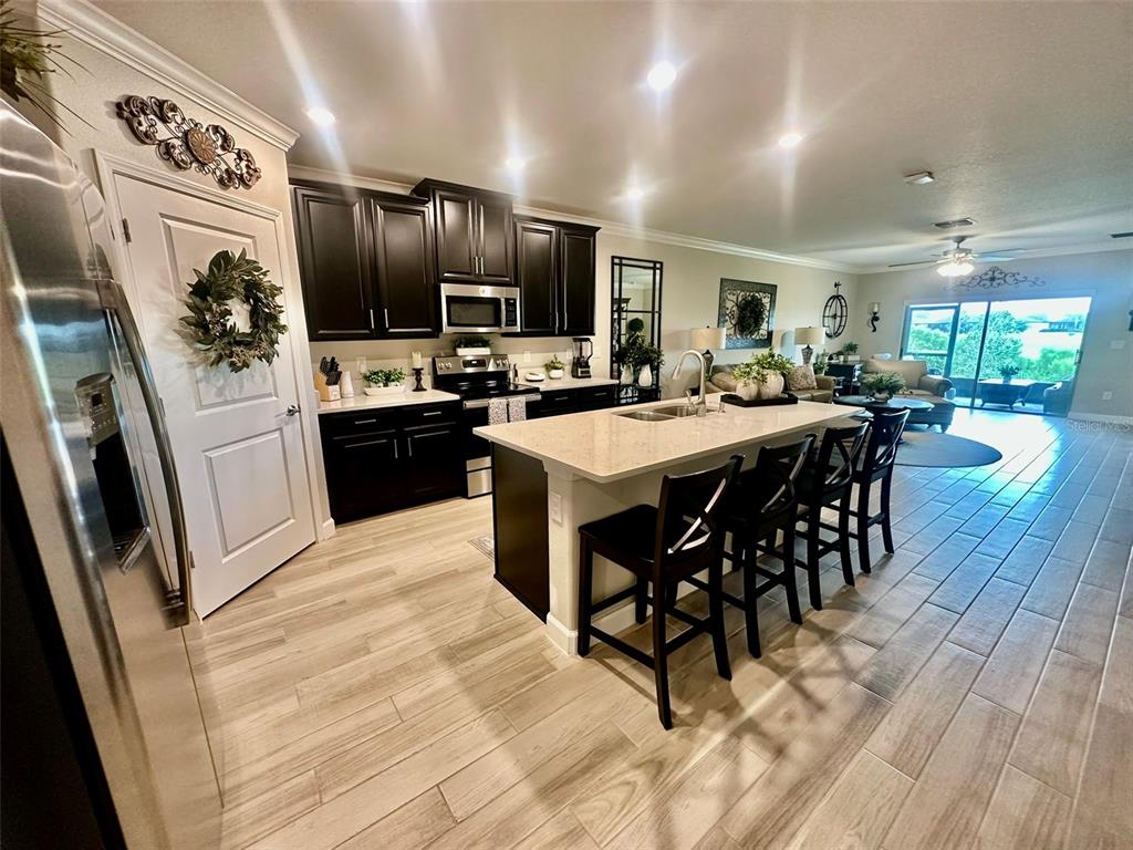 A kitchen with dark cabinets, a quartz-topped island, and light wood-look tile flooring — 10442 ECHO DOCK LOOP, SAN ANTONIO, FL