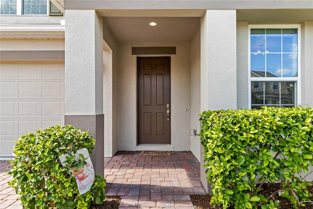 A front entrance with a brown door, brick walkway, and two green bushes — 5022 DOWN COURT, ST CLOUD, FL
