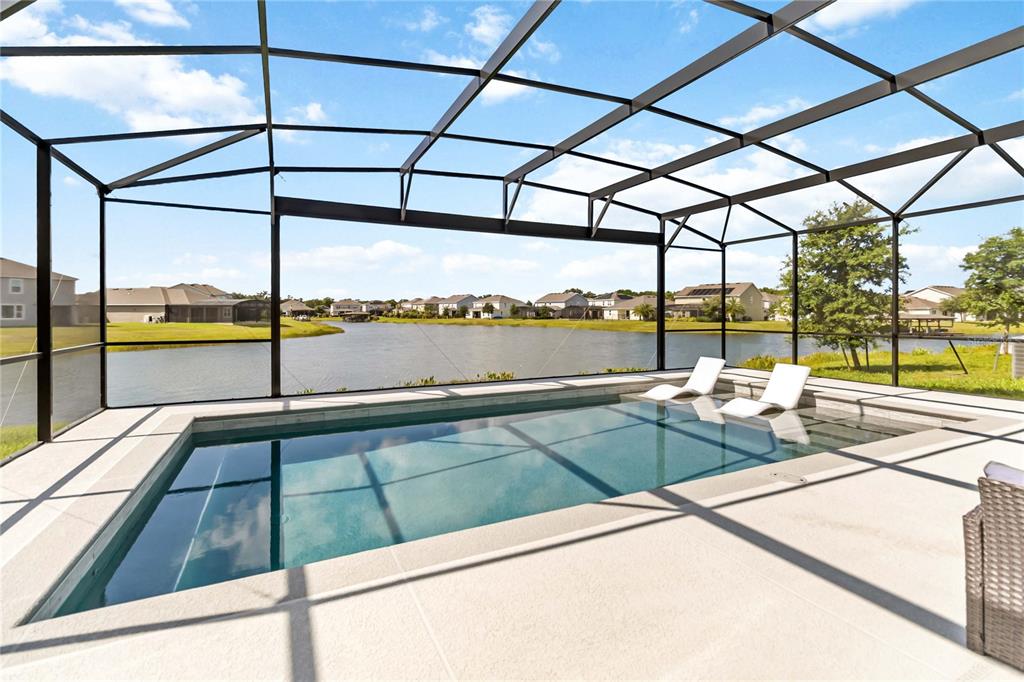 A screened-in pool patio overlooks a lake with two lounge chairs in the water — 5022 DOWN COURT, ST CLOUD, FL