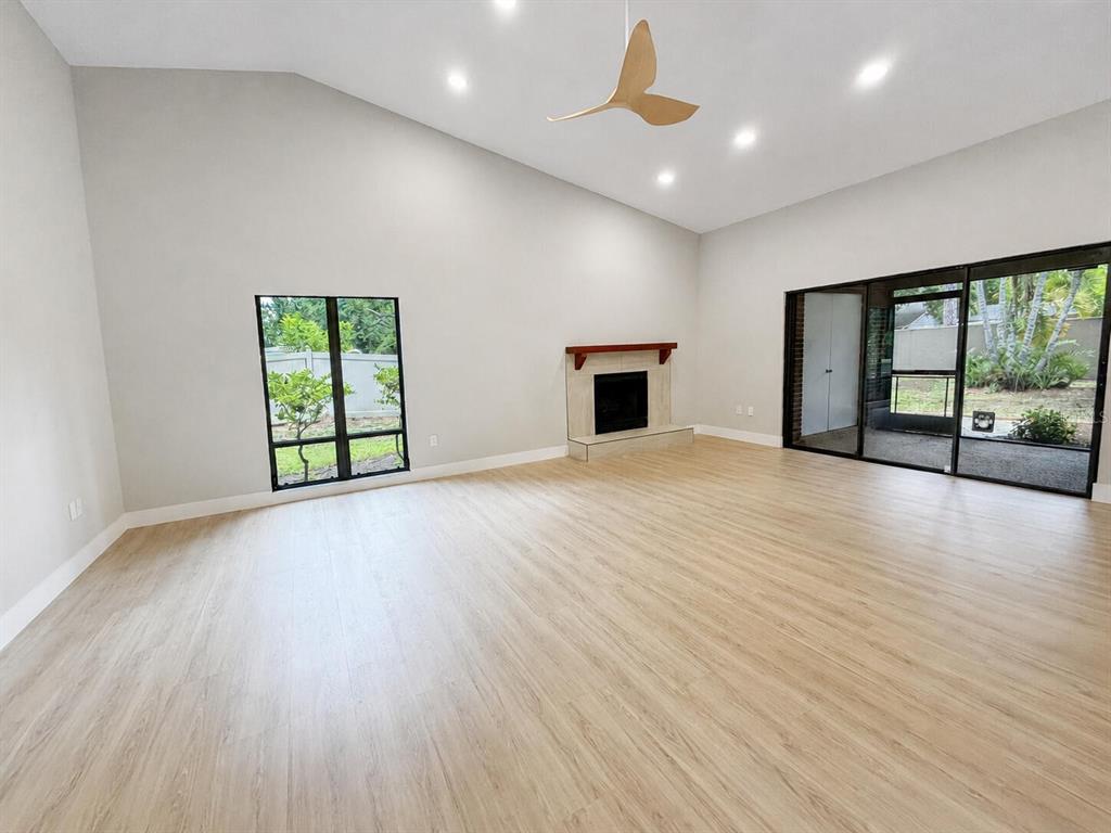 A spacious living room features light wood-look flooring, a vaulted ceiling, a fireplace, and sliding doors — 971 SUNRIDGE DRIVE UNIT 110, SARASOTA, FL