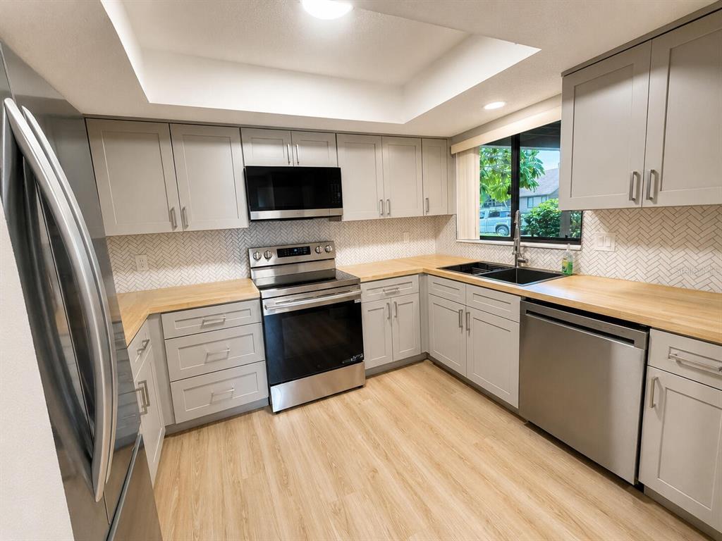 A kitchen with light gray cabinets, butcher block countertops, stainless steel appliances, and herringbone backsplash — 971 SUNRIDGE DRIVE UNIT 110, SARASOTA, FL