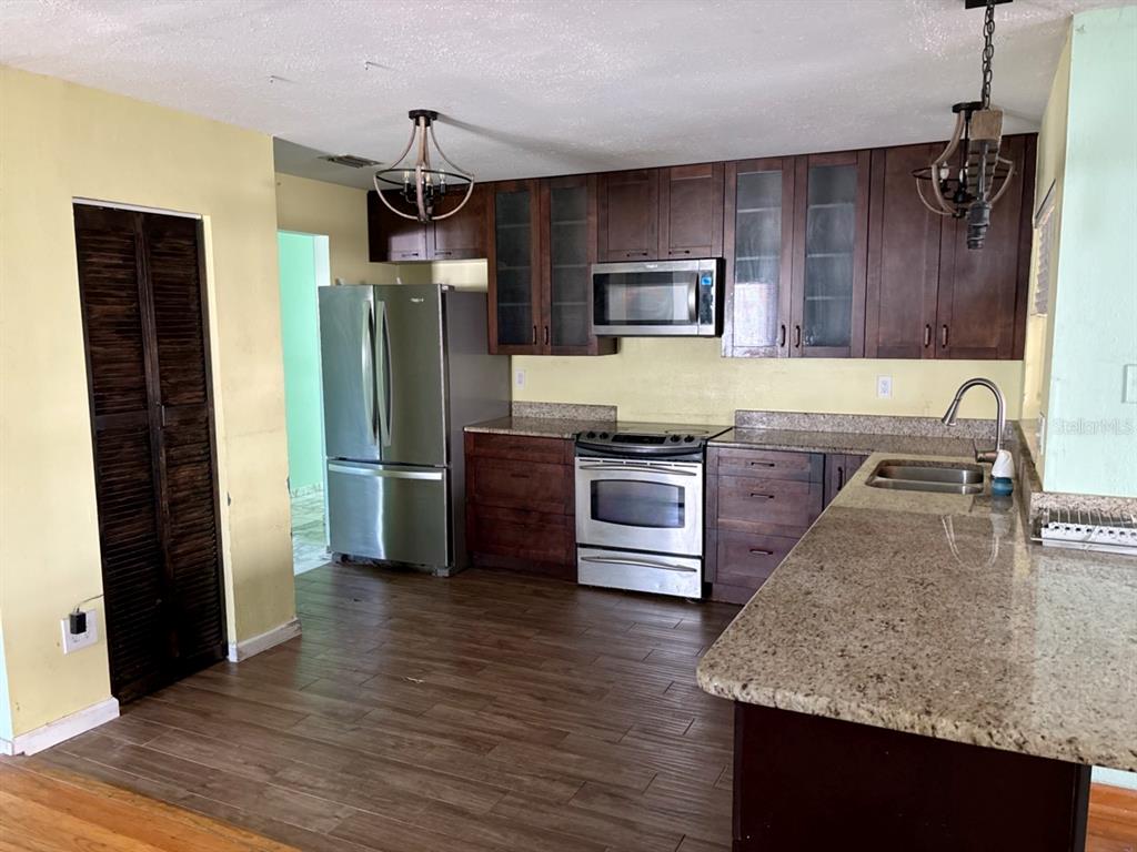 A kitchen features dark wood cabinets, stainless steel appliances, granite countertops, and wood-look tile flooring — 4604 RIDGE POINT, TAMPA, FL