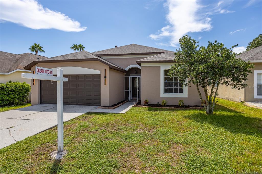 A single-story tan house with a brown garage door and a front yard — 22836 MARSH WREN DRIVE, LAND O LAKES, FL