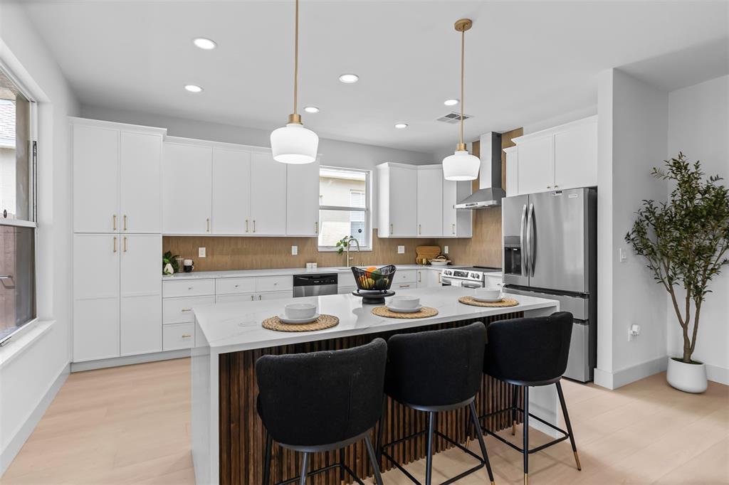 A modern kitchen features white cabinetry, a large marble-topped island, and three black bar stools — 22836 MARSH WREN DRIVE, LAND O LAKES, FL