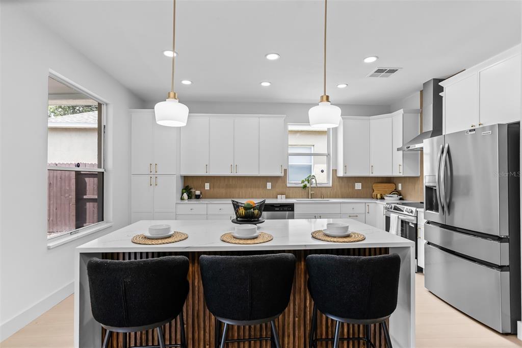 A modern kitchen features white cabinetry, a large island with three stools, and stainless appliances — 22836 MARSH WREN DRIVE, LAND O LAKES, FL