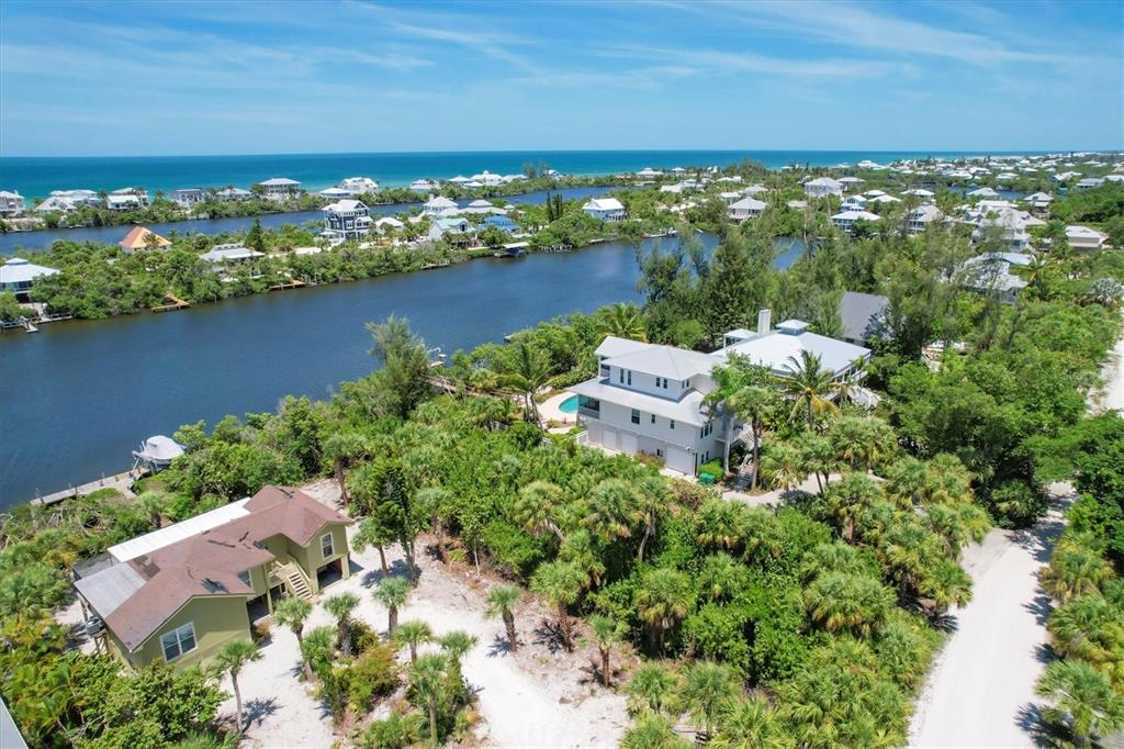 An aerial view shows two houses surrounded by lush vegetation near a canal and ocean — 211 KETTLE HARBOR DRIVE, PLACIDA, FL