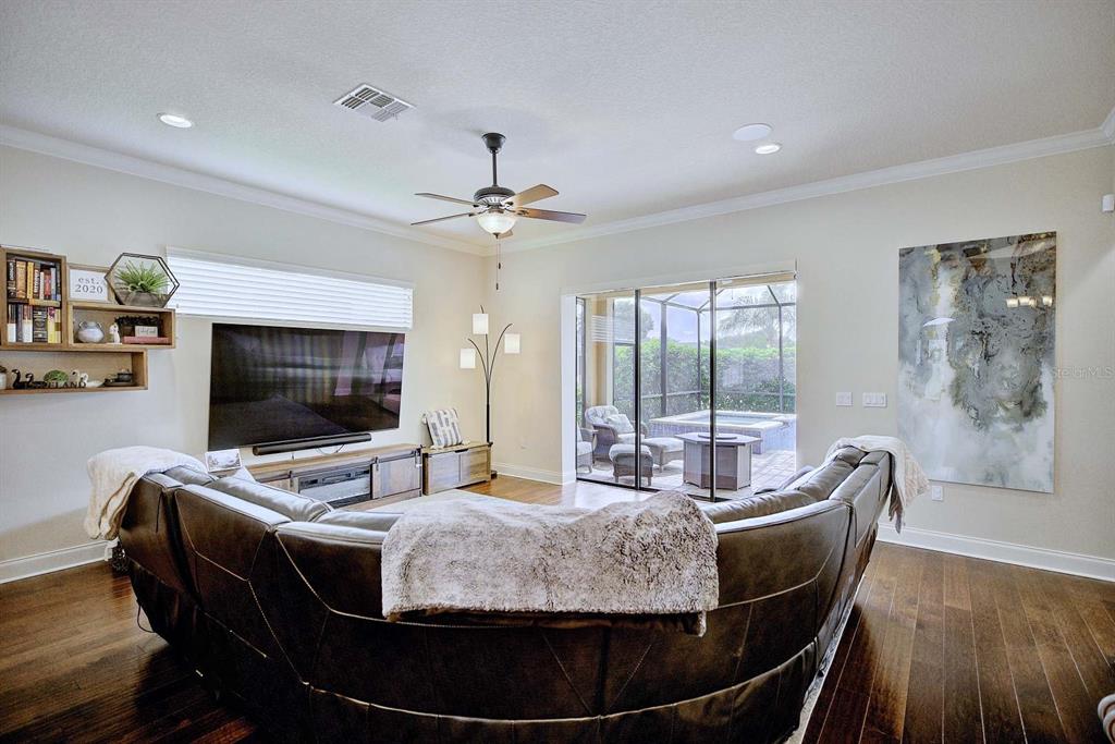 A living room features a large curved leather sofa, wood flooring, and sliding glass patio doors — 904 CHRISTINA CHASE LANE, LAKELAND, FL