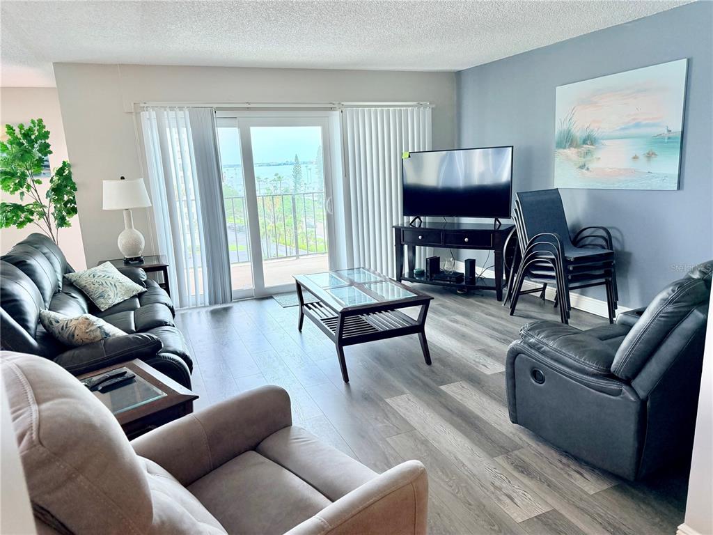 A living room features dark leather furniture, a glass-top coffee table, and a balcony view — 1480 GULF BOULEVARD UNIT 607, CLEARWATER BEACH, FL