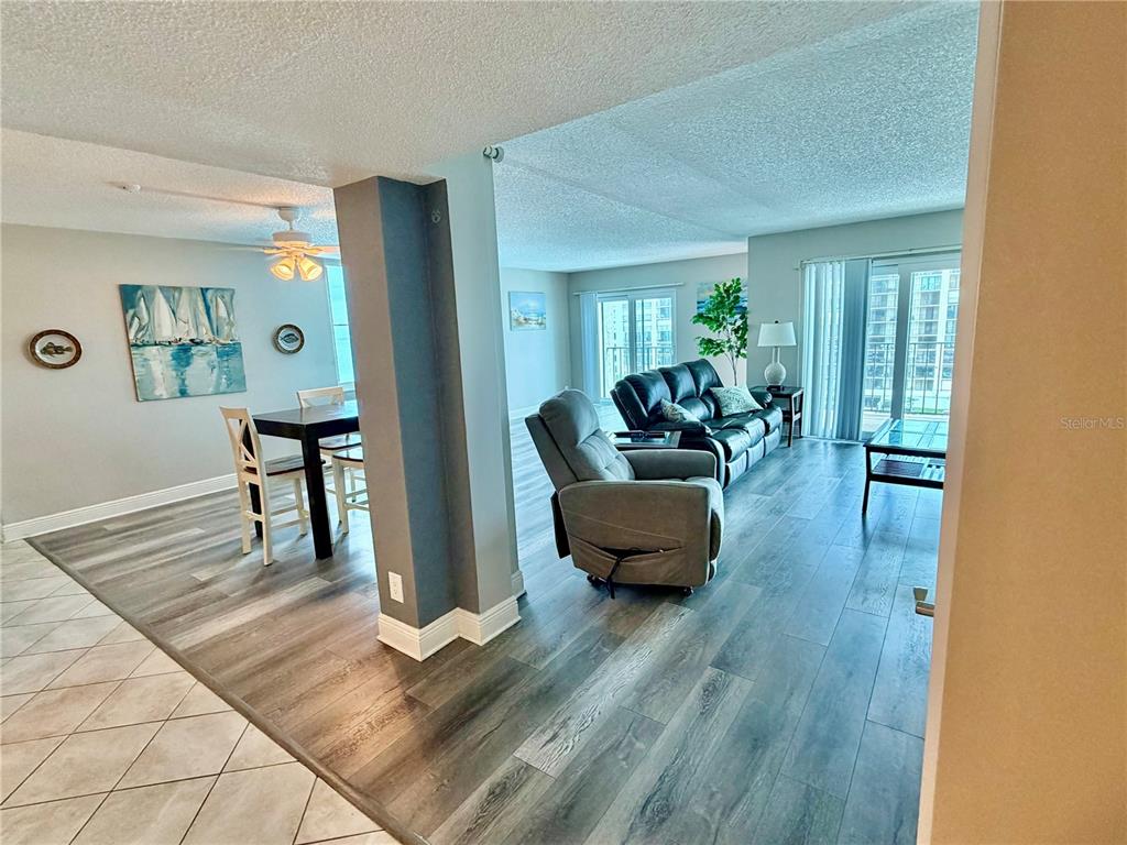 An open-concept living and dining area features wood-look flooring, a gray accent pillar, and balcony access — 1480 GULF BOULEVARD UNIT 607, CLEARWATER BEACH, FL