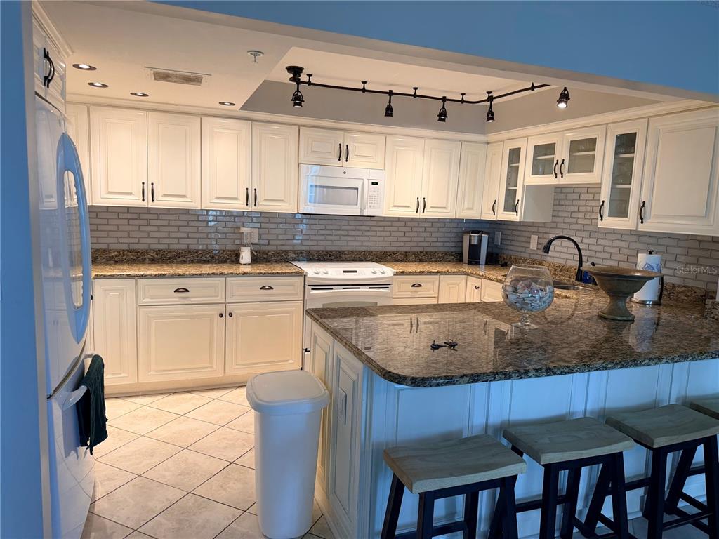 A kitchen features white cabinets, granite countertops, a subway tile backsplash, and a breakfast bar — 1480 GULF BOULEVARD UNIT 607, CLEARWATER BEACH, FL
