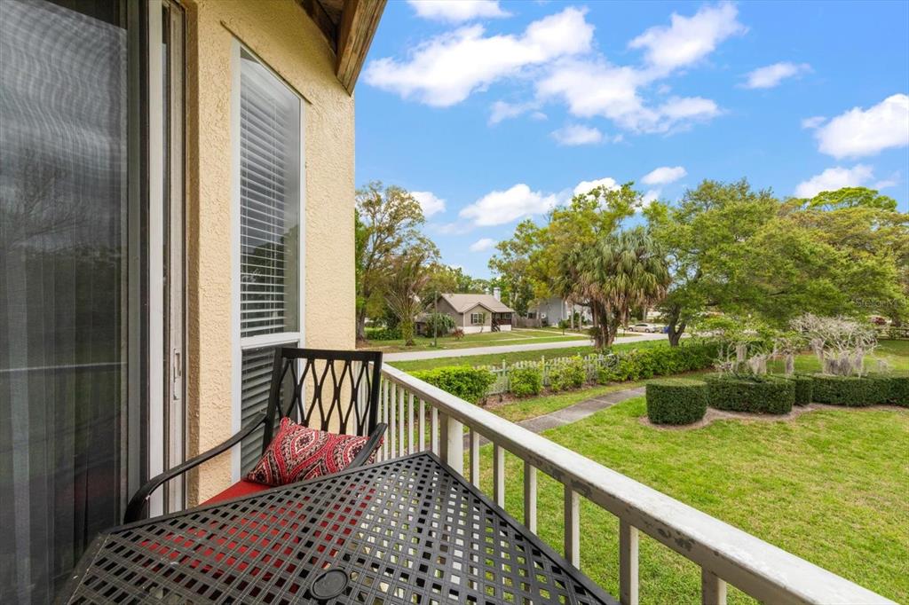 A balcony with a metal table and chair overlooks a grassy yard and neighborhood street — 108 BRENT CIRCLE, OLDSMAR, FL