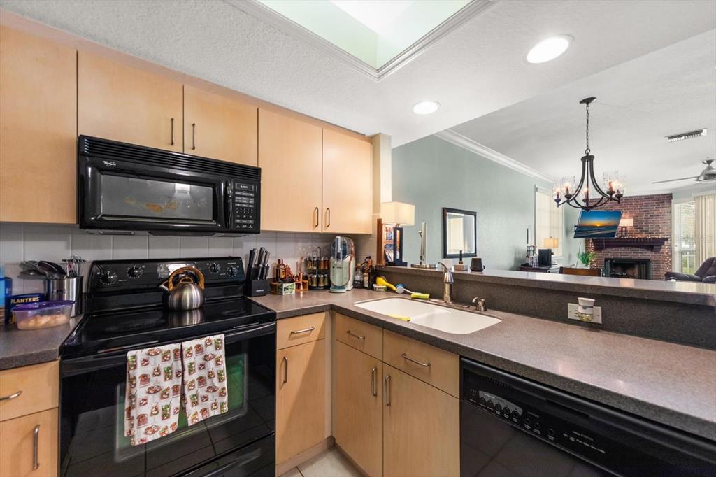 A kitchen with light wood cabinets, black appliances, and a view into the living area — 108 BRENT CIRCLE, OLDSMAR, FL