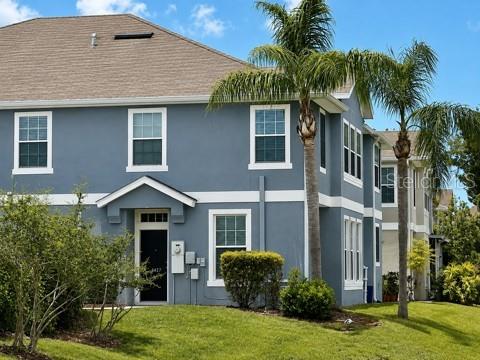 A two-story light green house features a stone-pillared gate and manicured landscaping — 8427 BLUE ROCK DRIVE, NEW PORT RICHEY, FL