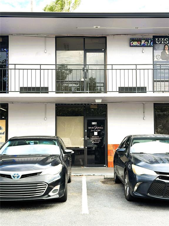 Two dark sedans are parked in front of a two-story commercial building with exterior walkways — 8421 S ORANGE BLOSSOM TRAIL UNIT 228, ORLANDO, FL