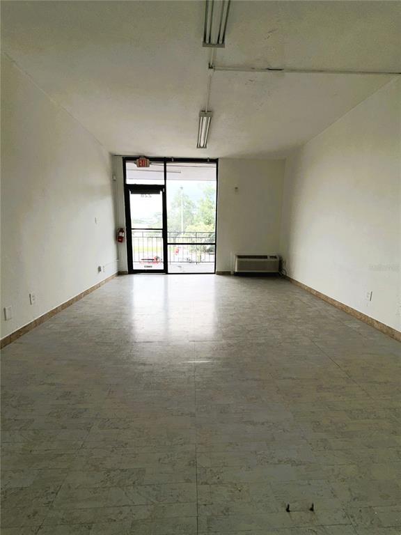 An empty commercial space features white walls, tiled flooring, a glass entrance door, and fluorescent lighting — 8421 S ORANGE BLOSSOM TRAIL UNIT 228, ORLANDO, FL