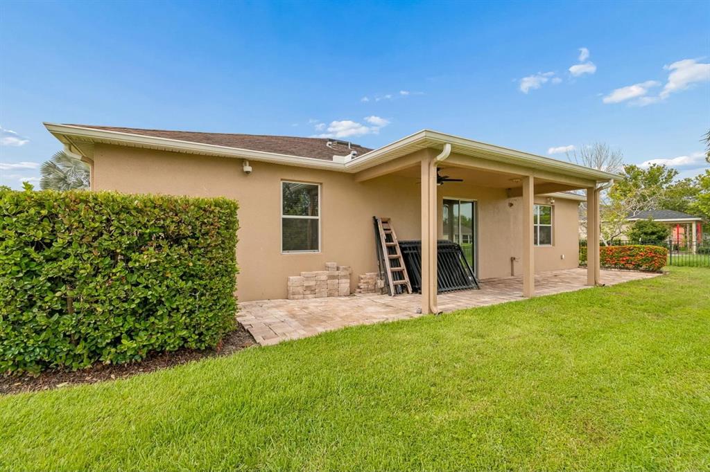 A tan house exterior features a covered patio, a paved floor, and a large hedge — 5406 SANDY SHELL DRIVE, APOLLO BEACH, FL