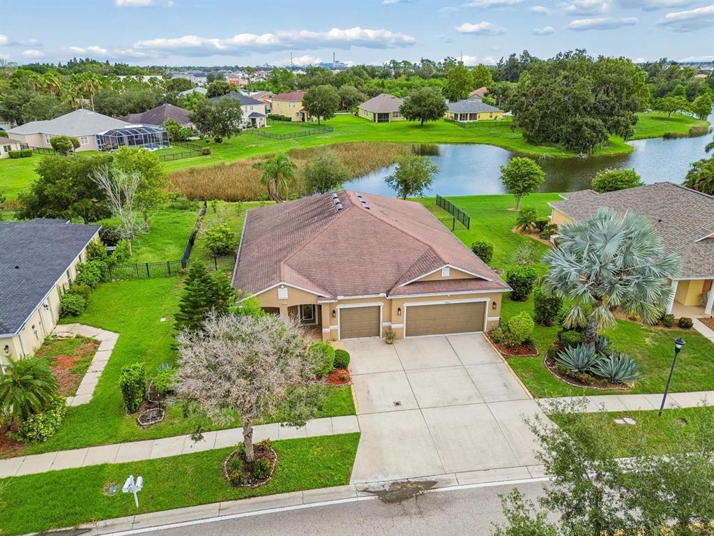 An aerial view shows a tan single-story house with a three-car garage and a pond — 5406 SANDY SHELL DRIVE, APOLLO BEACH, FL