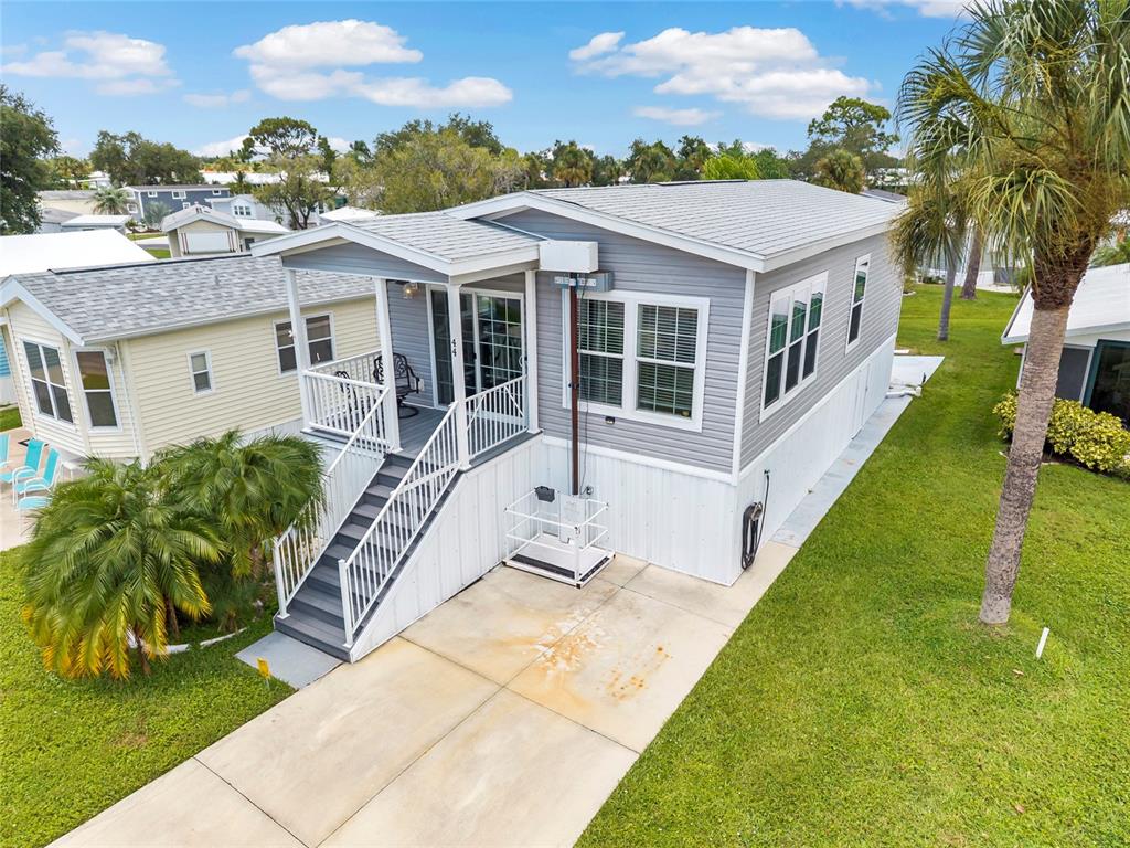 An elevated gray manufactured home features a front porch, stairs, and a wheelchair lift — 44 CROWN POINT DRIVE, NOKOMIS, FL
