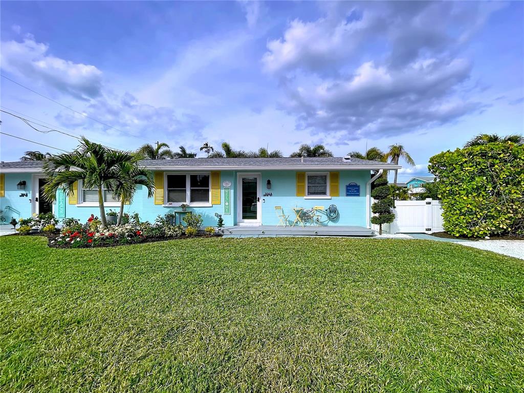 A light blue single-story house with yellow shutters and a front lawn under a cloudy sky — 304 29TH STREET UNIT A, HOLMES BEACH, FL