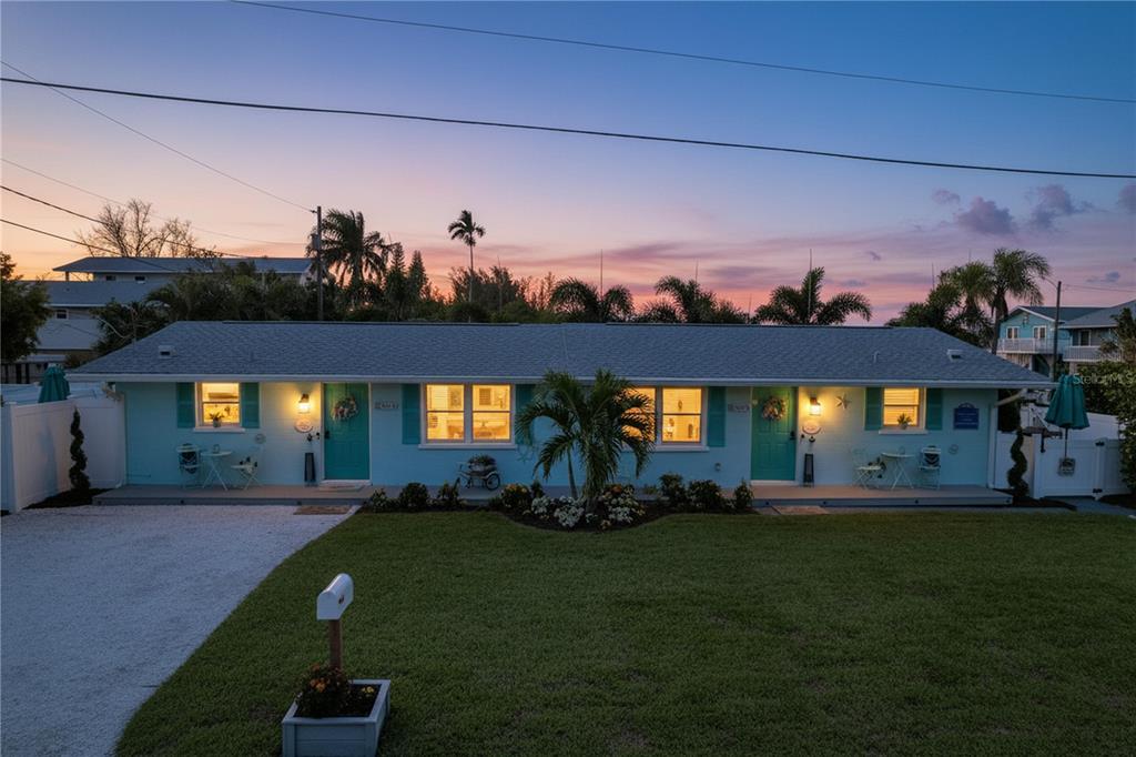 A single-story, light blue duplex with teal doors and a gravel driveway at sunset — 304 29TH STREET UNIT A, HOLMES BEACH, FL
