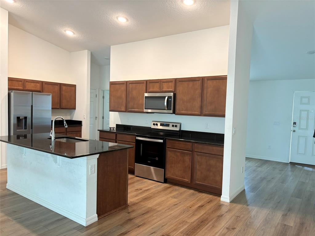 A kitchen features dark wood cabinets, black countertops, stainless steel appliances, and wood-look flooring — 15 LAMOYNE LANE, PALM COAST, FL