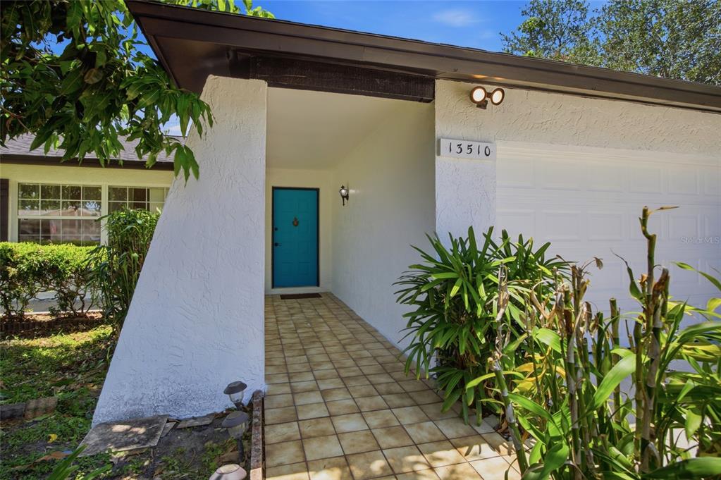 A white house exterior features a bright blue front door and a tiled walkway — 13510 CAPITOL DRIVE, TAMPA, FL