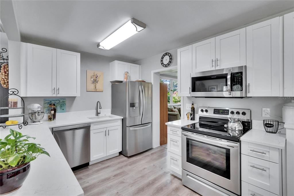 A kitchen with white cabinets, stainless steel appliances, and light wood-look flooring — 1623 SAN MATEO DRIVE, DUNEDIN, FL