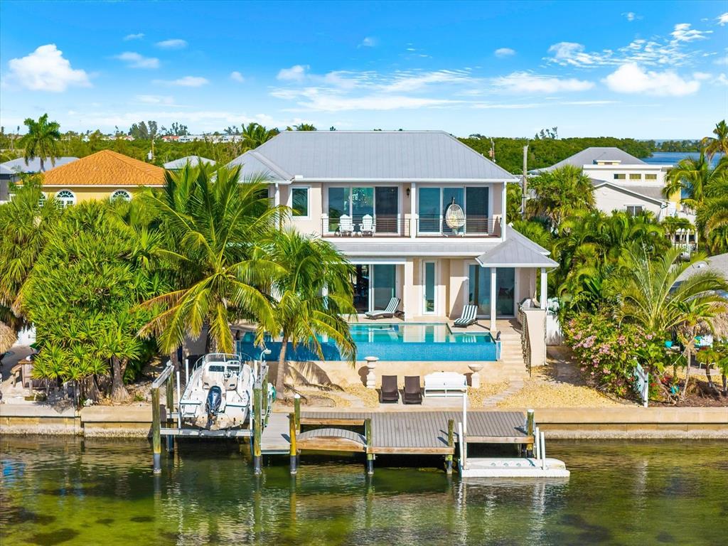 A two-story waterfront house features a swimming pool, a boat lift, and a wooden dock — 511 BAYVIEW DRIVE, HOLMES BEACH, FL