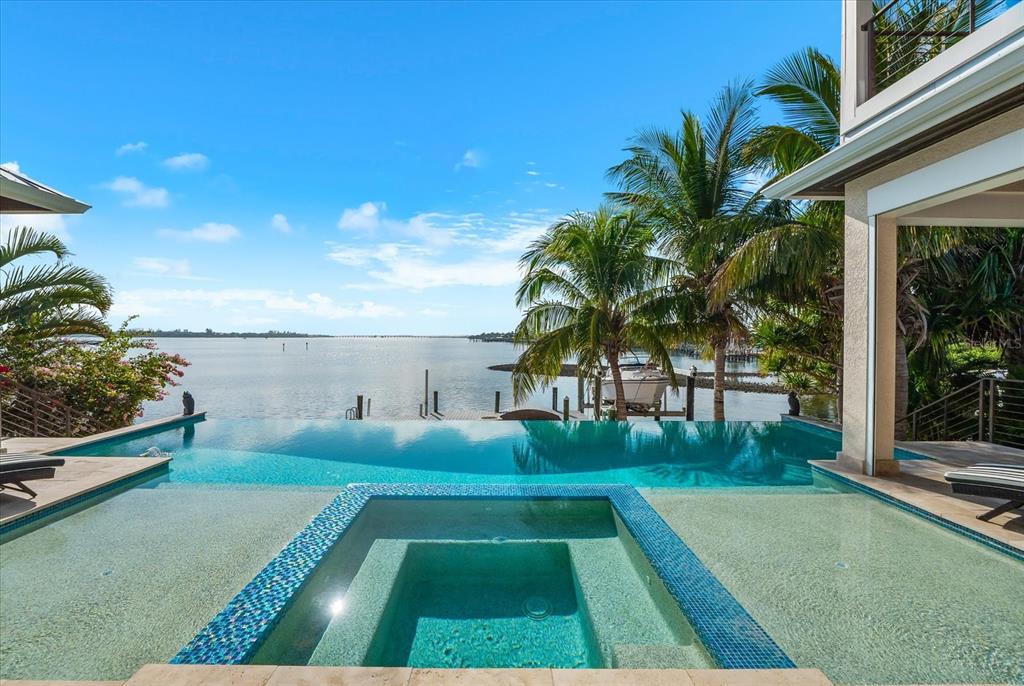 An infinity pool and spa overlook a bay with palm trees and a boat dock — 511 BAYVIEW DRIVE, HOLMES BEACH, FL