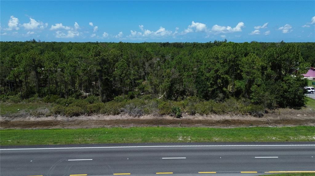 An aerial view shows a paved road bordering a grassy strip and a wooded lot — 12209 12215 12219 12225 TAMIAMI TRAIL, PUNTA GORDA, FL