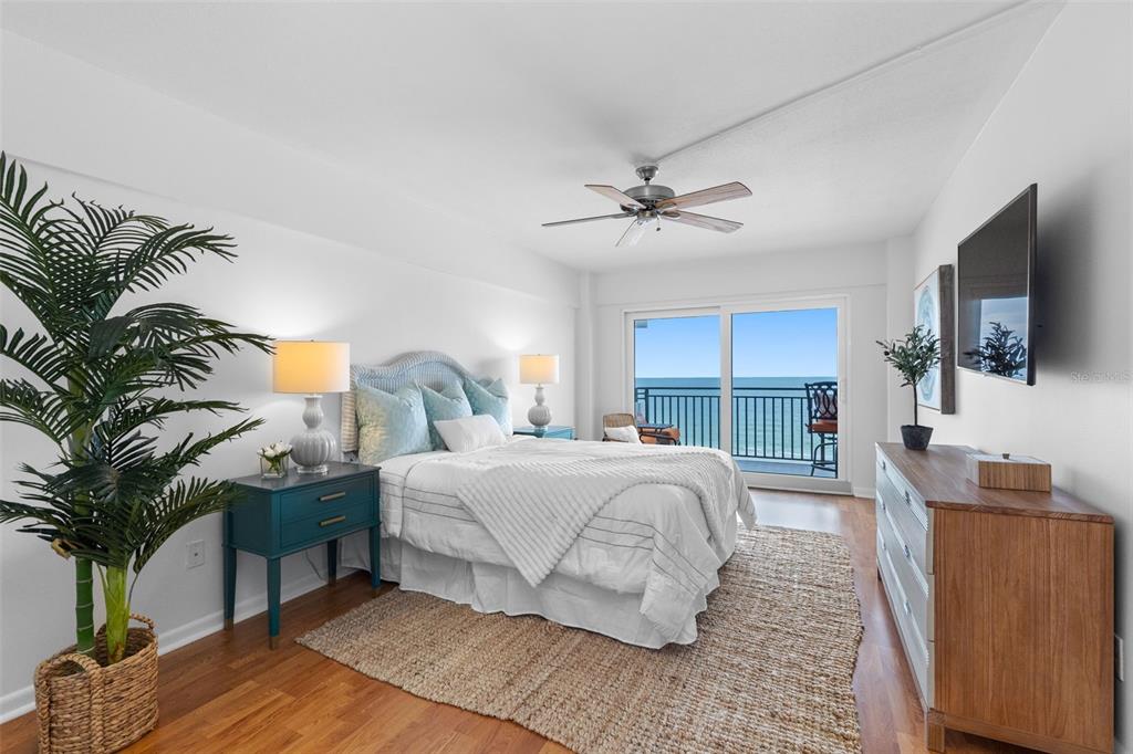 A bedroom features a bed, a teal nightstand, a wooden dresser, and a balcony with ocean views — 1310 GULF BOULEVARD UNIT 503, INDIAN ROCKS BEACH, FL