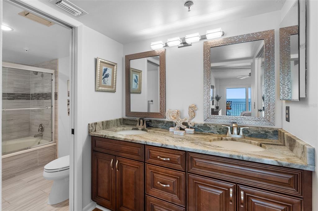 A bathroom features a double vanity with granite countertops, dark wood cabinets, and two mirrors — 1310 GULF BOULEVARD UNIT 503, INDIAN ROCKS BEACH, FL