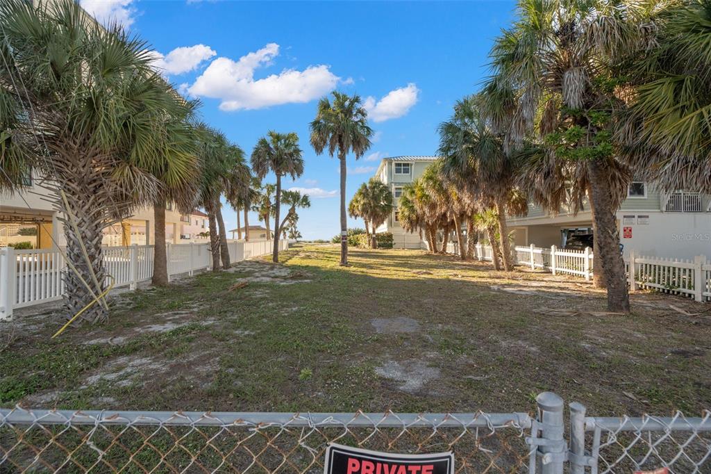 A vacant, sandy lot sits between two multi-story buildings, lined with palm trees and white fences — 1306 GULF BOULEVARD, INDIAN ROCKS BEACH, FL