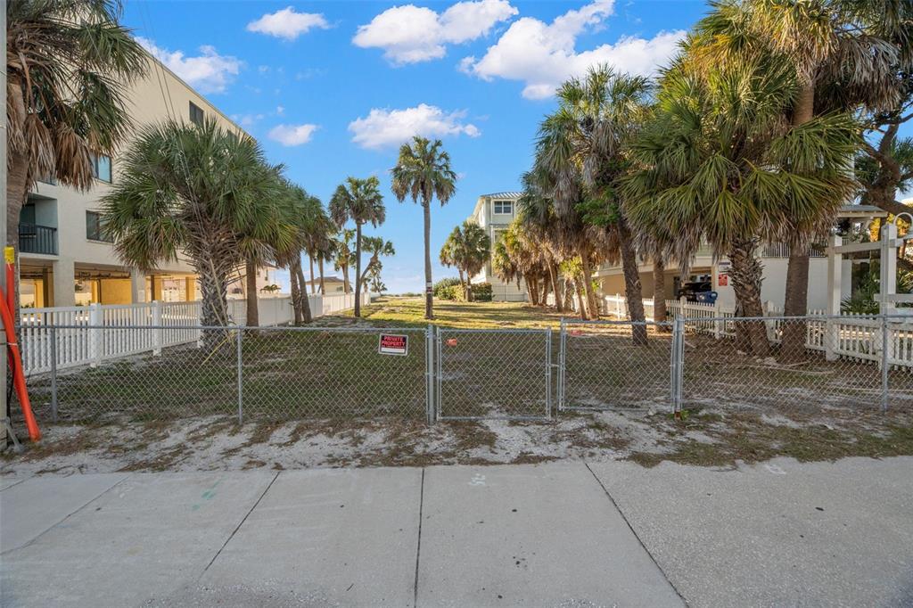 A chain-link fence encloses a vacant sandy lot lined with palm trees between two buildings — 1306 GULF BOULEVARD, INDIAN ROCKS BEACH, FL