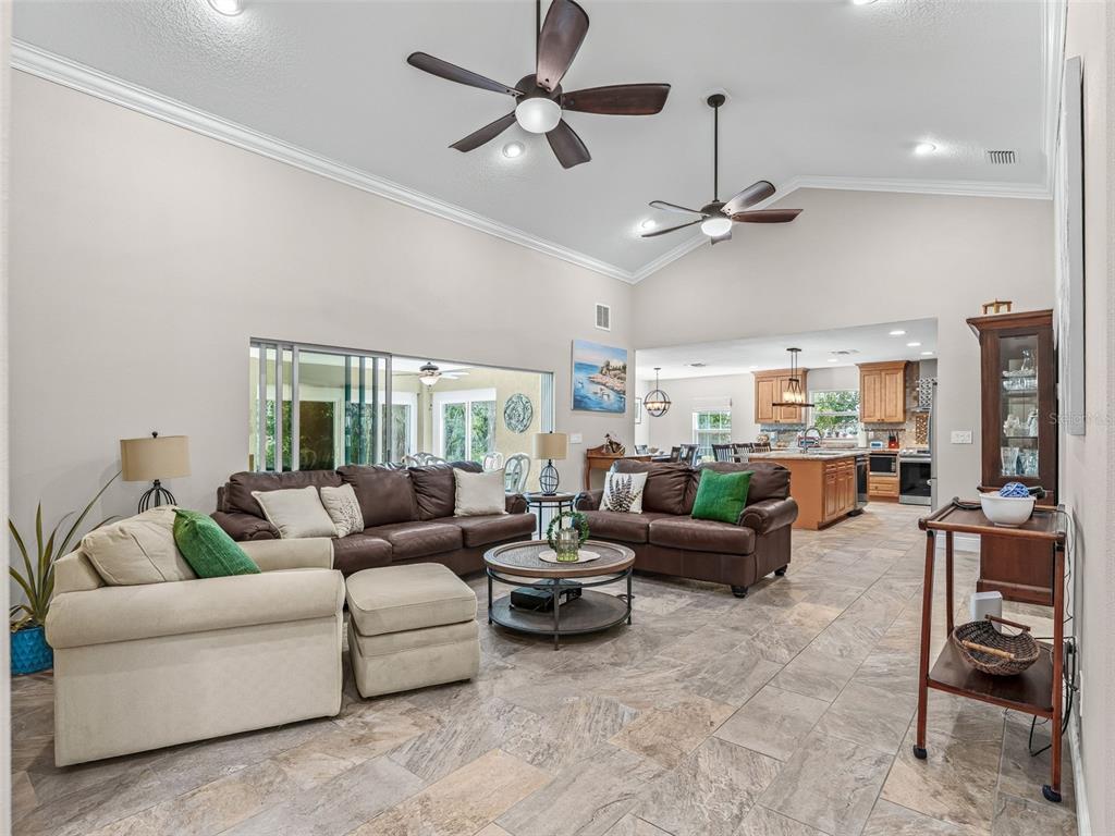 A living room with vaulted ceilings, tile floors, and an open view into the kitchen — 5331 GROVE MANOR, LADY LAKE, FL