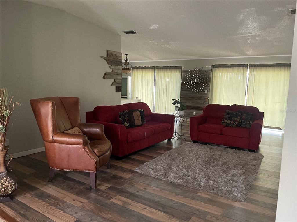 A living room features wood-look flooring, two red sofas, a leather armchair, and a rug — 1601 STEPHENS ROAD, RUSKIN, FL