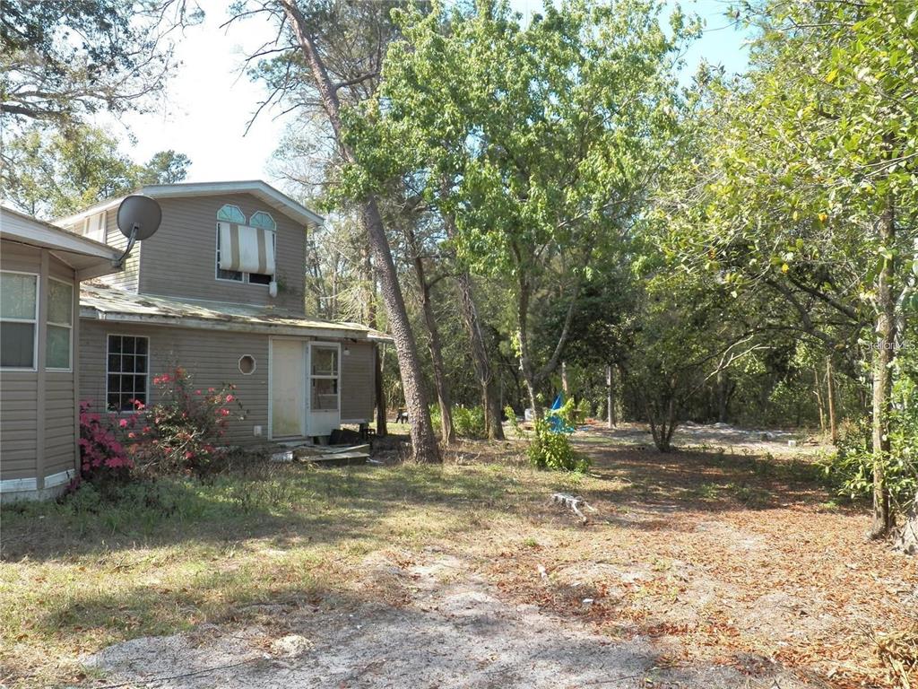 A two-story house with tan siding stands in a wooded yard with scattered leaves — 15730 GIFFORD LANE, SPRING HILL, FL