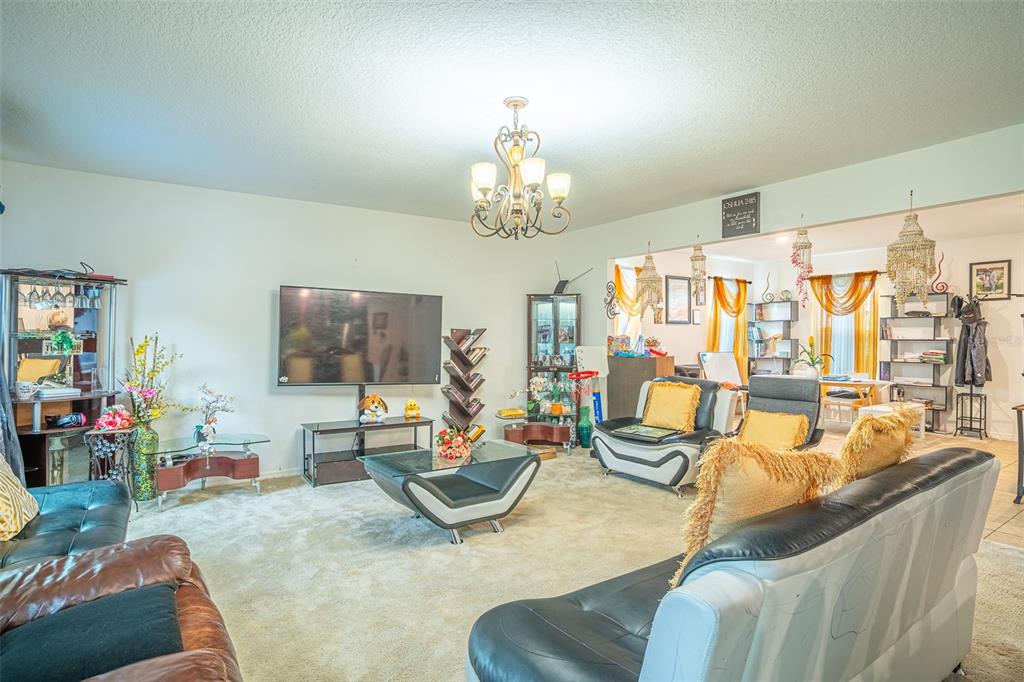 A living room with beige carpet, a television, a chandelier, and several pieces of furniture — 15107 ZENITH AVENUE, MASCOTTE, FL