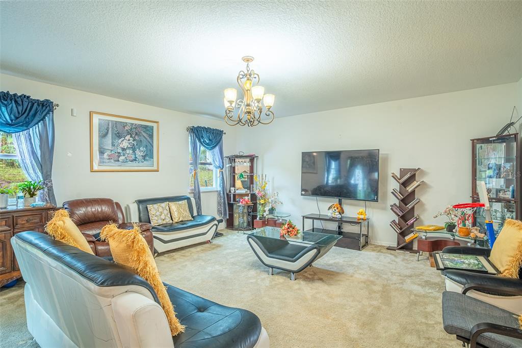 A living room features a large television, a chandelier, and several pieces of leather furniture — 15107 ZENITH AVENUE, MASCOTTE, FL