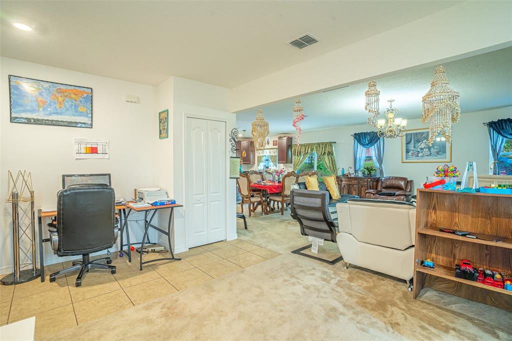 A home office area with tile flooring transitions into a carpeted living room and dining area — 15107 ZENITH AVENUE, MASCOTTE, FL