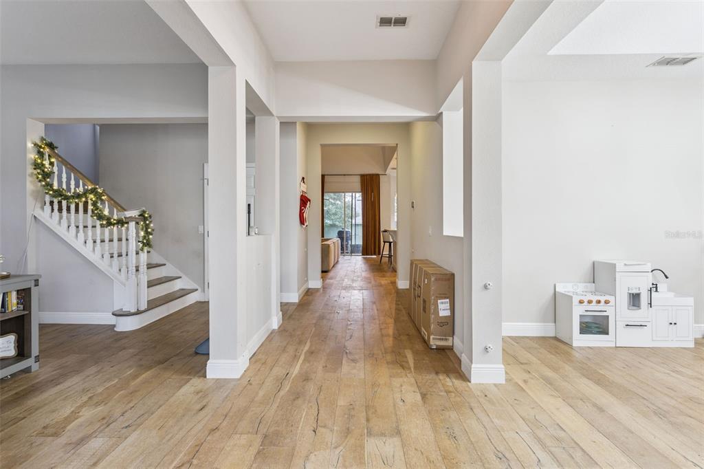 A bright entryway features light wood flooring, a staircase with garland, and an open layout — 3443 TUMBLING RIVER DRIVE, CLERMONT, FL